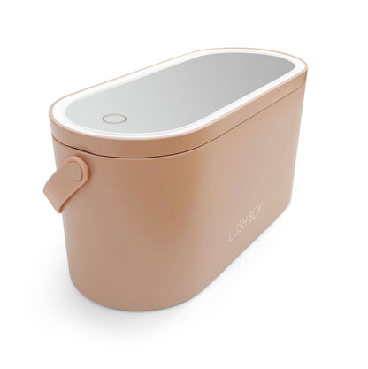 The Rio Lush Box Vanity Case is a rectangular beige case with rounded edges, a reflective lid, and a circular top button. Featuring a side handle and LUSH BOX print, its your perfect travel companion for stylish organization.