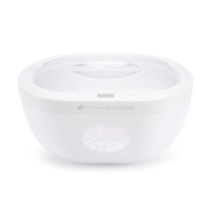 The Rio Paraffin Wax Heater is a white, oval-shaped device with a transparent lid, small digital display, and subtle branding, designed for comfort and skin hydration. Shown against a plain white background.